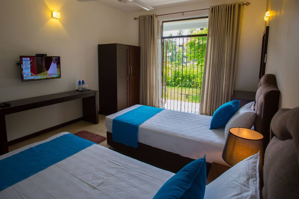 Habitación de hotel con dos camas, un escritorio, un televisor y vistas a zonas verdes.