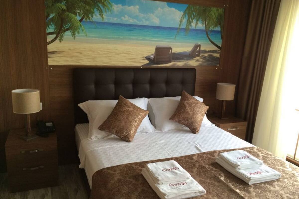 A hotel room with a bed, two pillows, a nightstand, a lamp, and a painting of a beach scene.