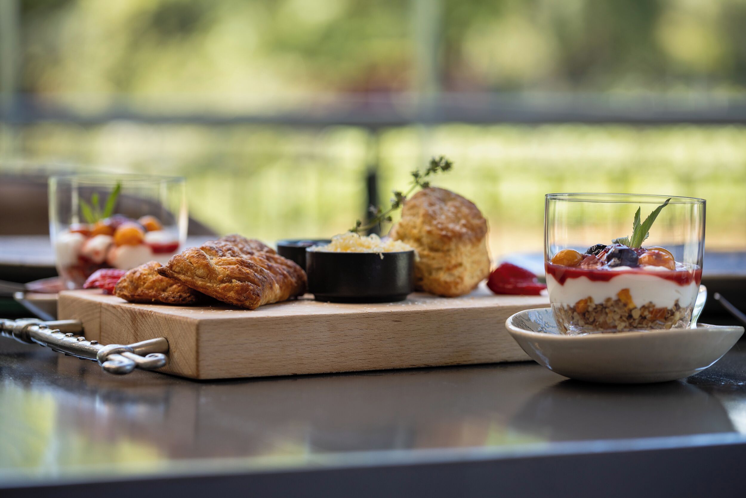 A breakfast setting with pastries, a bowl of yogurt, and a glass of fruit on a wooden board.