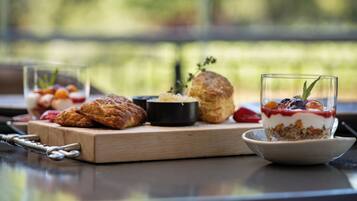 A breakfast setting with pastries, a bowl of yogurt, and a glass of fruit on a wooden board.