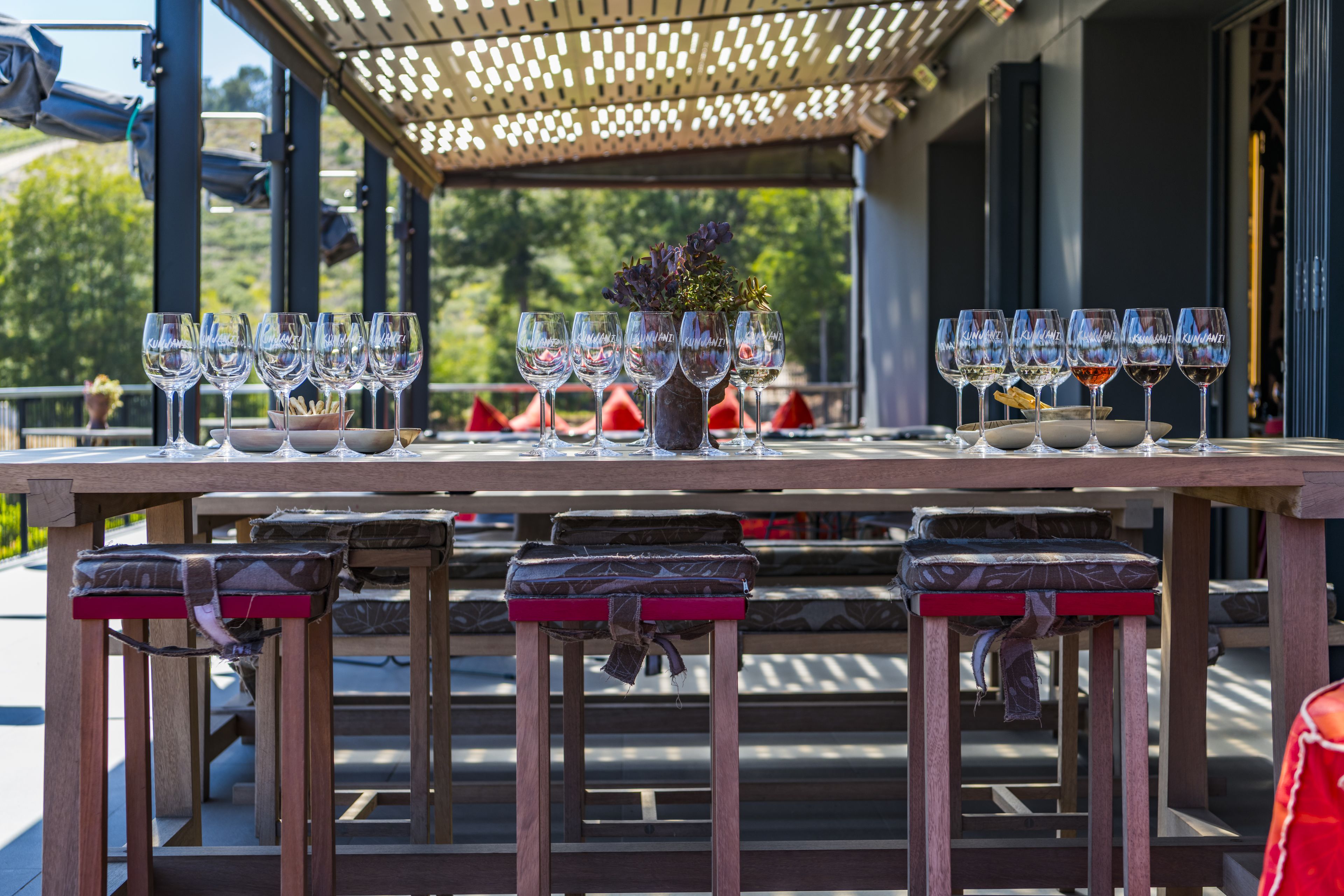 A table set with wine glasses and a centerpiece, outdoors with a pergola overhead.