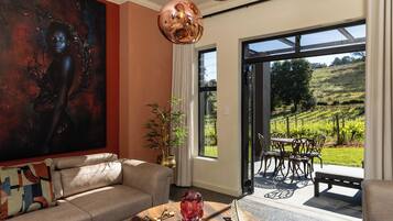 A modern living room with a large painting, a sofa, a coffee table with decorative items, and a view of a vineyard through a glass door.