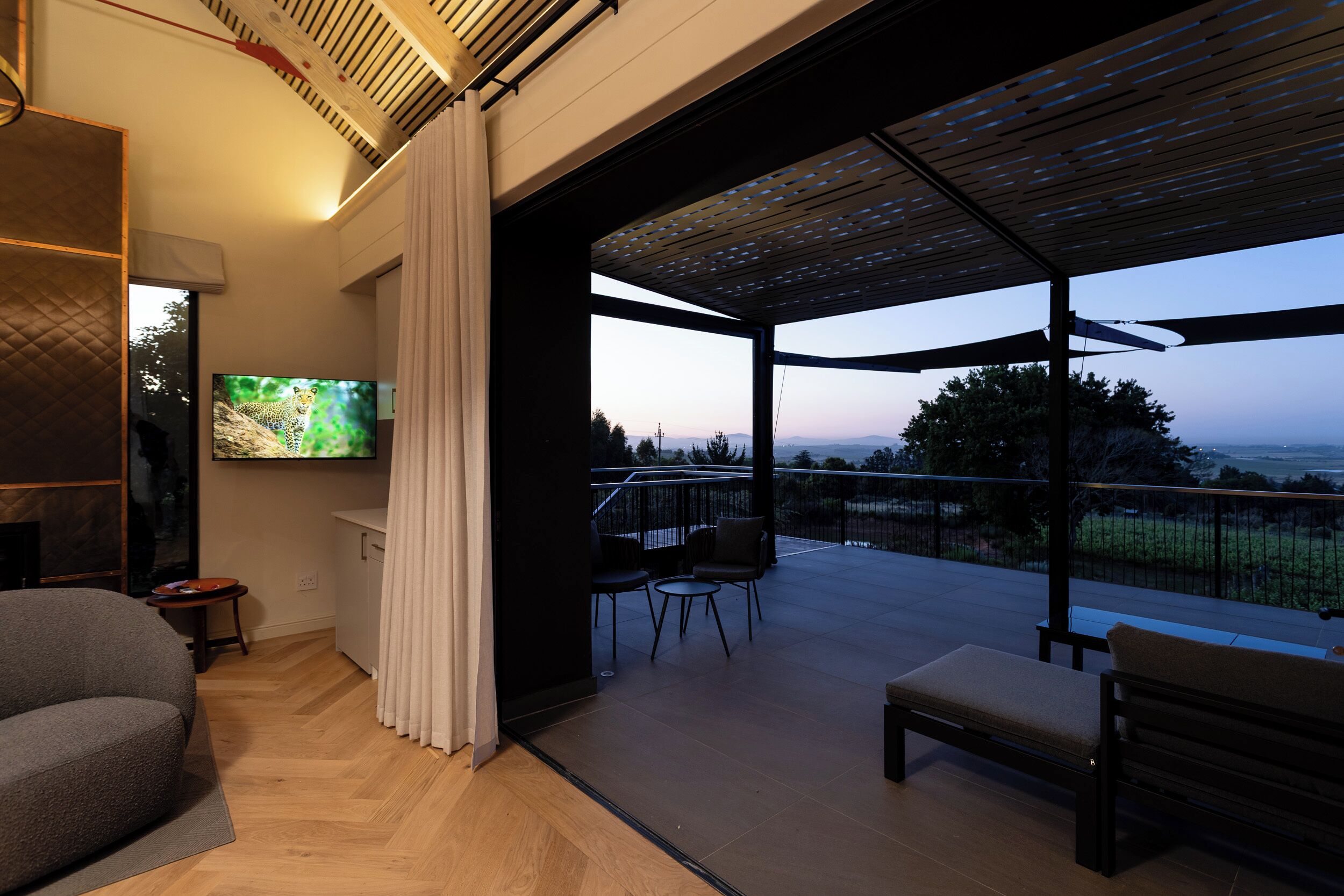 A modern living room with a flat-screen TV, a sofa, and a balcony with outdoor seating.