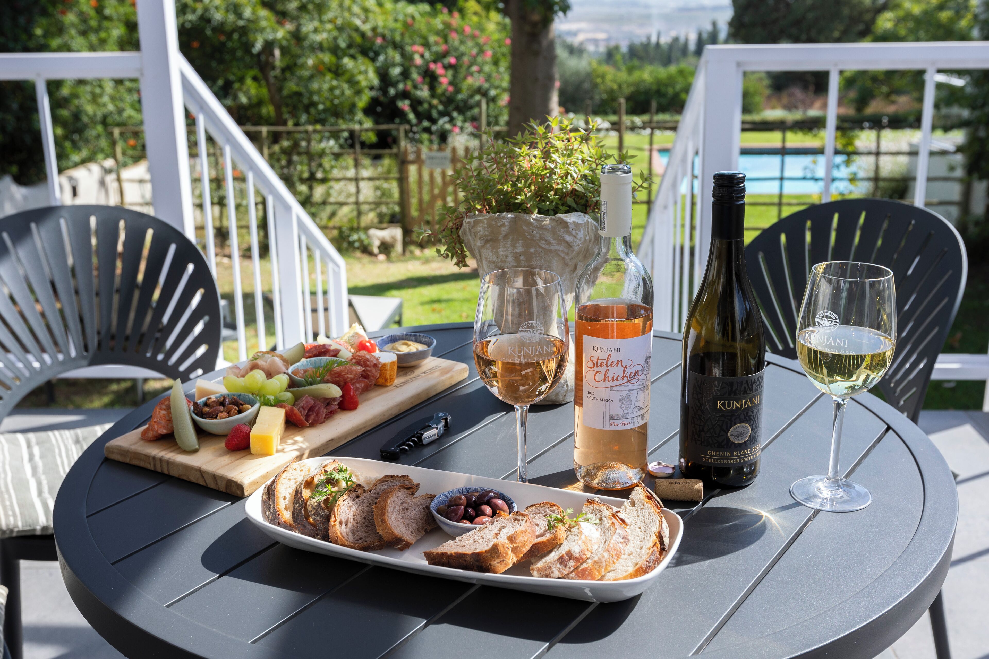 Une table dressée à l’extérieur, avec une bouteille de vin, un verre, une assiette de nourriture et un bol d’olives.