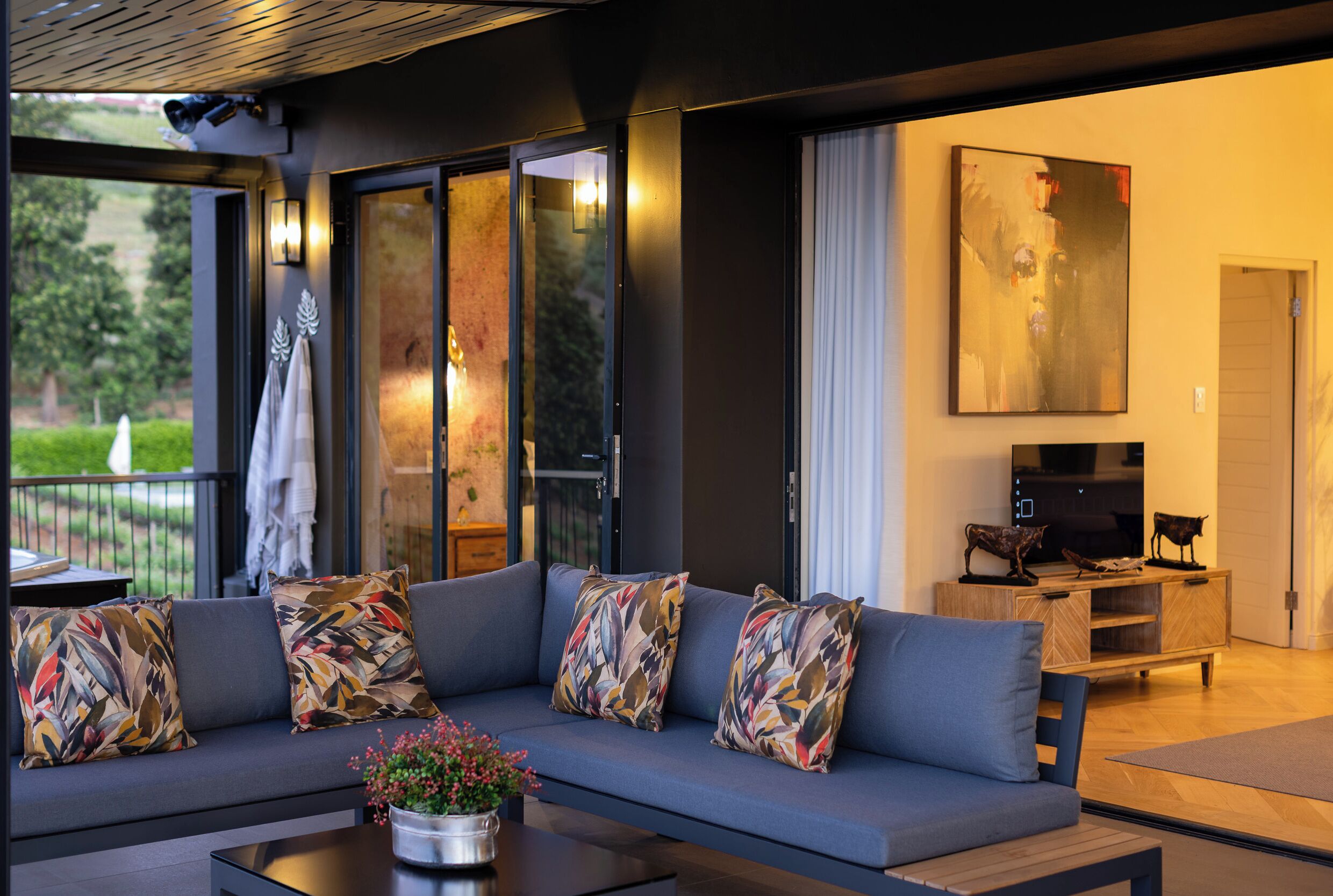 A modern living room with a grey sofa, colorful cushions, a coffee table with a flower vase, and a wooden TV stand.