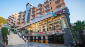 A multi-story hotel with a glass facade, outdoor seating area, and a staircase leading to the entrance. - Diamond Hill (Vlorë)