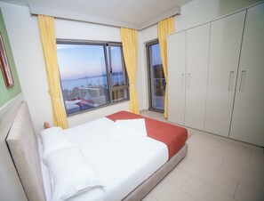 Quarto de hotel com cama, guarda-roupa e vista para o mar pela janela.