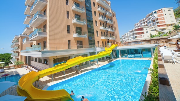 A modern hotel with a pool, a yellow water slide, and multiple balconies. - Diamond Hill (Vlorë)