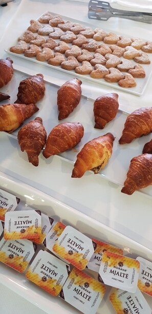 Exibição de doces, incluindo biscoitos em formato de coração, croissants e embalagens de leite com mel.
