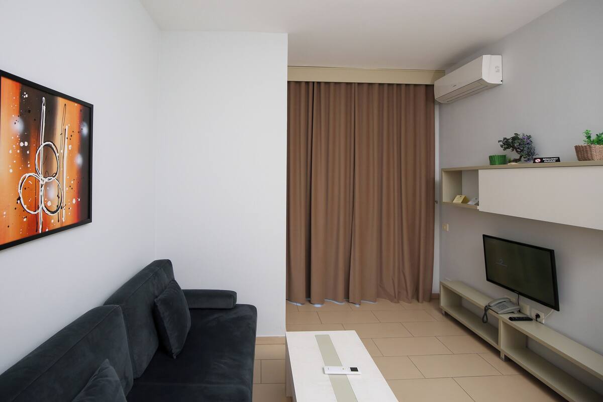 Un salon moderne avec un canapé noir, un téléviseur à écran plat, une table basse blanche et un climatiseur fixé au mur.