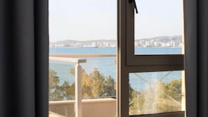 A room with a large window offering a view of a body of water and distant buildings. - Diamond Hill (Vlorë)