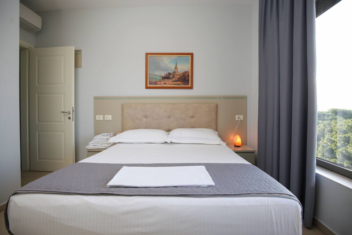Un lit bien fait, avec une couette blanche et des oreillers, une table de chevet avec une lampe et un tableau accroché au mur.