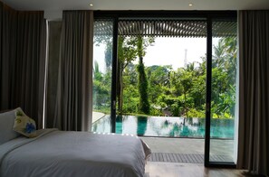 A bedroom with a large bed, a view of a swimming pool, and a lush garden outside. - 4 bedroom private pool villa (Ubud)