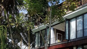 En moderne toetagers bygning med store vinduer og en balkon, omgivet af frodig vegetation og sprudlende tagetesblomster.