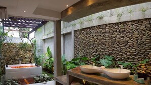 Et spa-område med stenvæg, stor skålsink og forskellige planter.