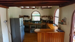 Een kleine keuken met een koelkast, houten aanrecht en een raam met tralies.