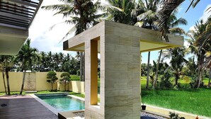 A modern outdoor pool area with a concrete structure, surrounded by lush greenery and palm trees. - RC Ubud Villa 1 (Ubud)