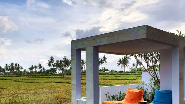 A modern outdoor seating area with a pool, surrounded by a lush green landscape and palm trees. - RC Ubud Villa 1 (Ubud)