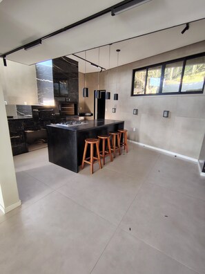 A modern kitchen with a central island, bar stools, pendant lights, and a large window.