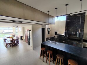 A modern kitchen with a black marble countertop, bar stools, and pendant lighting.