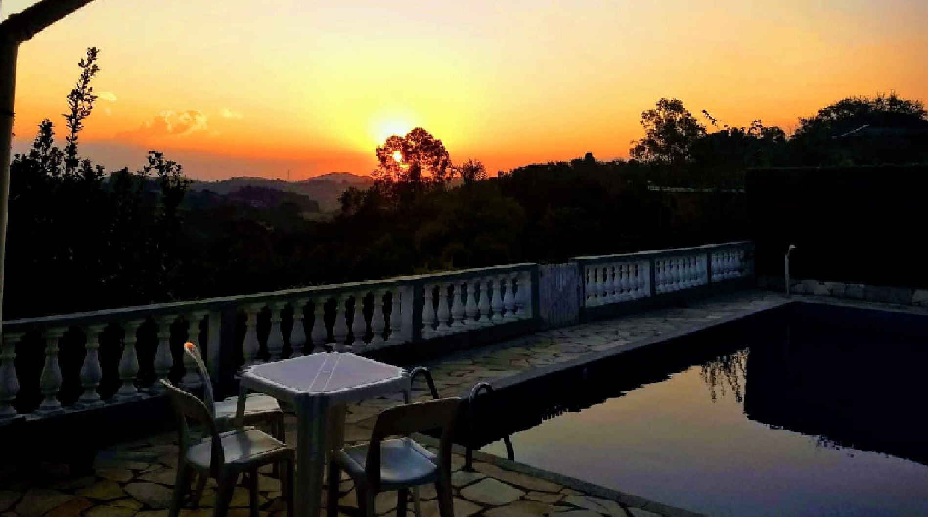 Um pátio com mesa e cadeiras, dando vista para a água e um pôr do sol.