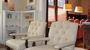 A living room with two upholstered chairs, a white shelving unit, and a door leading to another room. - Spacious, Historical, Magical, Designer Home, Prime Walkable Village Location! (Bar Harbor)