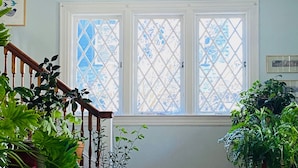 A room with a staircase, a large window with a lattice design, and various potted plants. - Spacious, Historical, Magical, Designer Home, Prime Walkable Village Location! (Bar Harbor)