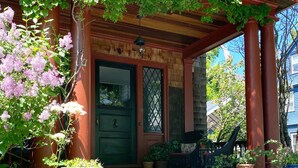 A traditional house with a wooden porch, a green door, and a brick wall. - Spacious, Historical, Magical, Designer Home, Prime Walkable Village Location! (Bar Harbor)