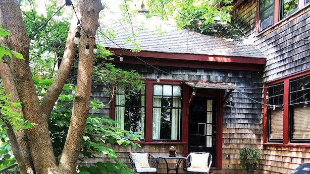 A rustic wooden house with a deck, outdoor seating, and a large tree in the foreground. - Spacious, Historical, Magical, Designer Home, Prime Walkable Village Location! (Bar Harbor)