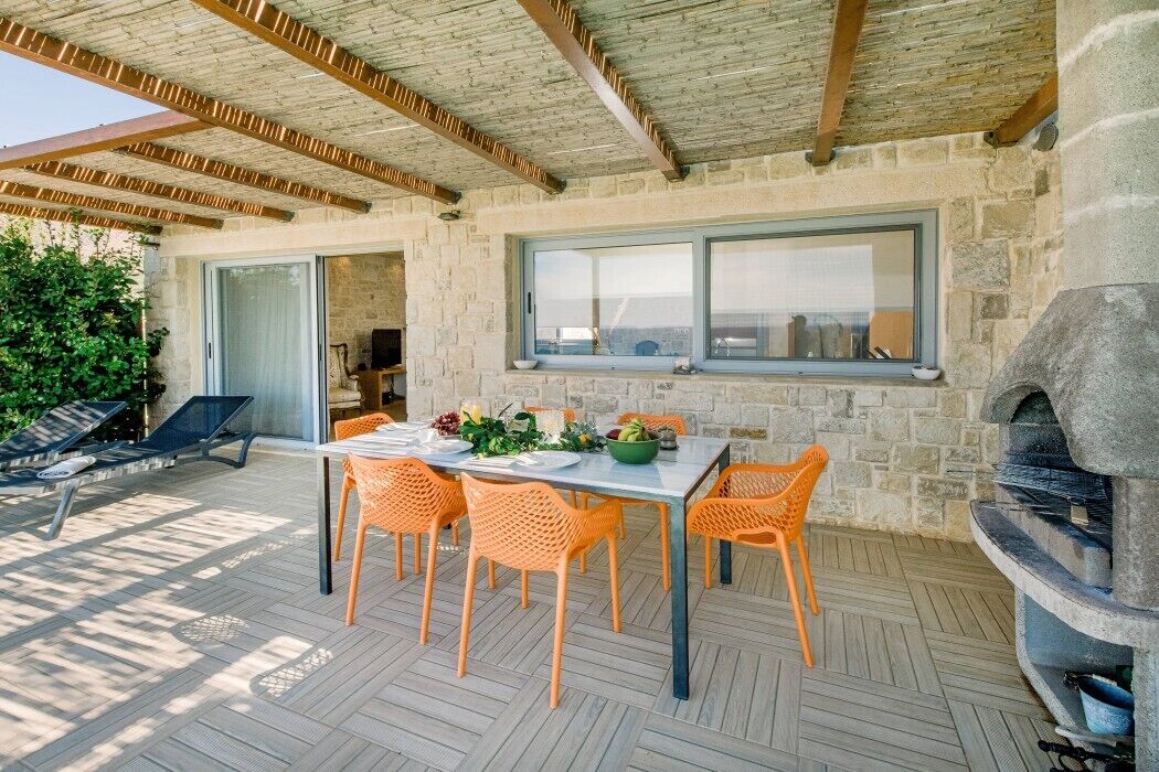 Une terrasse extérieure avec un mur en pierre, une table dressée pour le repas et un barbecue encastré.