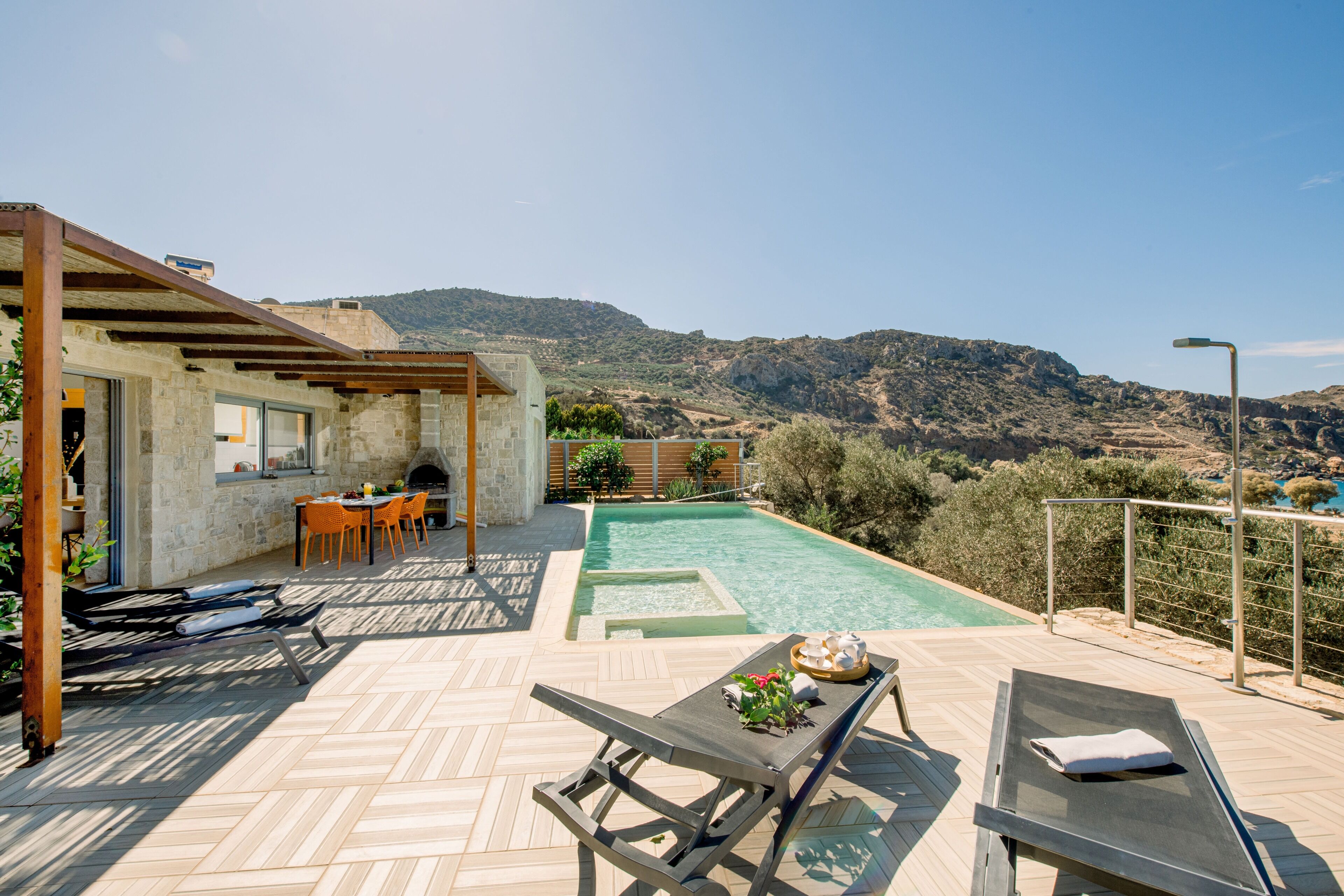 A pool area with a view of the mountains, a covered seating area, and a barbecue setup.