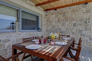 Comedor con paredes de piedra y un amplio ventanal con vista al mar, una mesa de madera dispuesta para dos personas y un techo rústico.