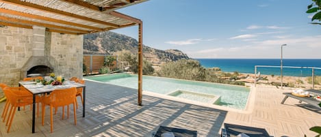 A patio with a stone fireplace, a pool, and a view of the sea.