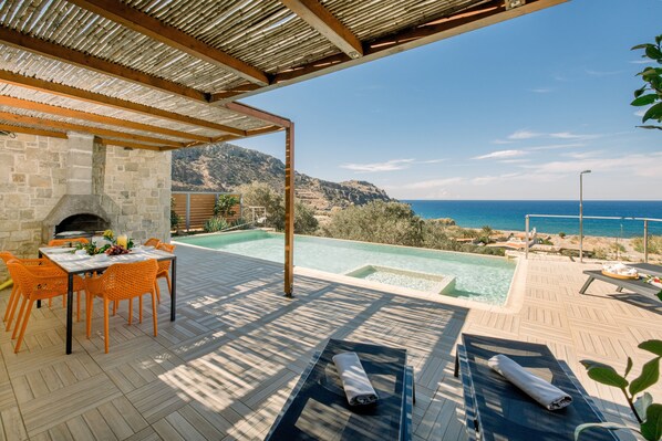 A patio with a stone fireplace, a pool, and a view of the sea.