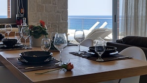 Une table à manger dressée avec des verres à vin, des assiettes et un arrangement floral au centre, donnant sur l’océan.