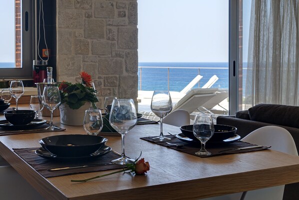 A dining table set with wine glasses, plates, and a flower centerpiece, overlooking the ocean.