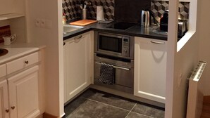 A compact kitchen with white cabinetry, a microwave, an oven, and a coffee maker. - Small house, completely reniewed, at the back of a silent yard, with trees. (Paris)