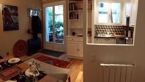 A living room with a dining area, a bookshelf, and a kitchen with a window. - Small house, completely reniewed, at the back of a silent yard, with trees. (Paris)