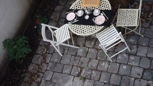 A round outdoor table with white chairs, set on a cobblestone patio. - Small house, completely reniewed, at the back of a silent yard, with trees. (Paris)