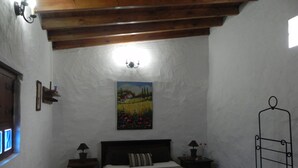 A bedroom with a wooden bed frame, a single bedside table with a lamp, a wall-mounted shelf, and a painting of a field. - Nice country house with terrace, sea and mountains views (Tigaday)