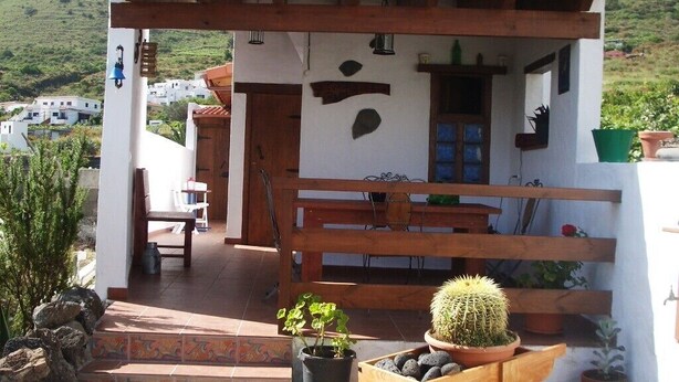 A rustic outdoor seating area with a wooden bench, a small table, and a wooden cart with a cactus. - Nice country house with terrace, sea and mountains views (Tigaday)