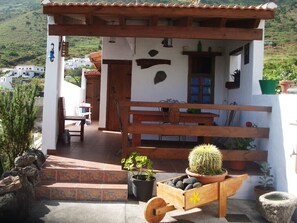 A rustic outdoor seating area with a wooden bench, a small table, and a wooden cart with a cactus. - Nice country house with terrace, sea and mountains views (Tigaday)