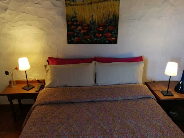 A bedroom with a bed, two bedside tables, lamps, a painting, and a red pillow. - Nice country house with terrace, sea and mountains views (Tigaday)