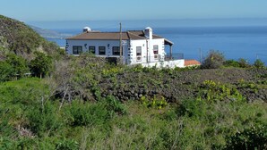 Une maison blanche avec un toit rouge, située sur une colline et offrant une vue sur l’océan.