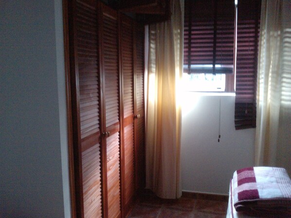 A room with wooden sliding doors, a window with blinds, and a bed with a checkered blanket.