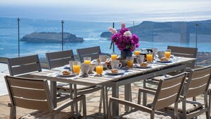 A table set for breakfast with orange juice, pastries, and a vase of flowers, overlooking a coastal view. - Mountain and Private Beach VILLA EAGLE  2-10 pers. (Chavgas)
