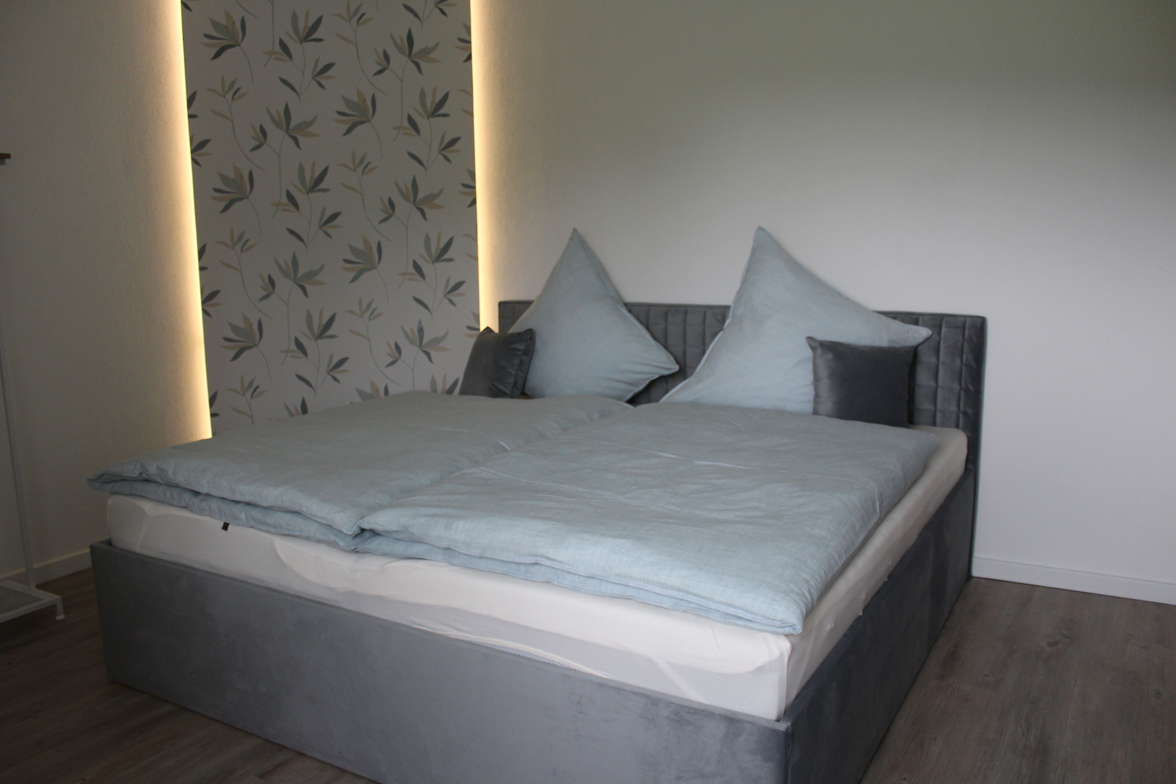 Ein modernes Schlafzimmer mit einem Bett, einem grauen Kopfteil und Wandtapete mit Muster.