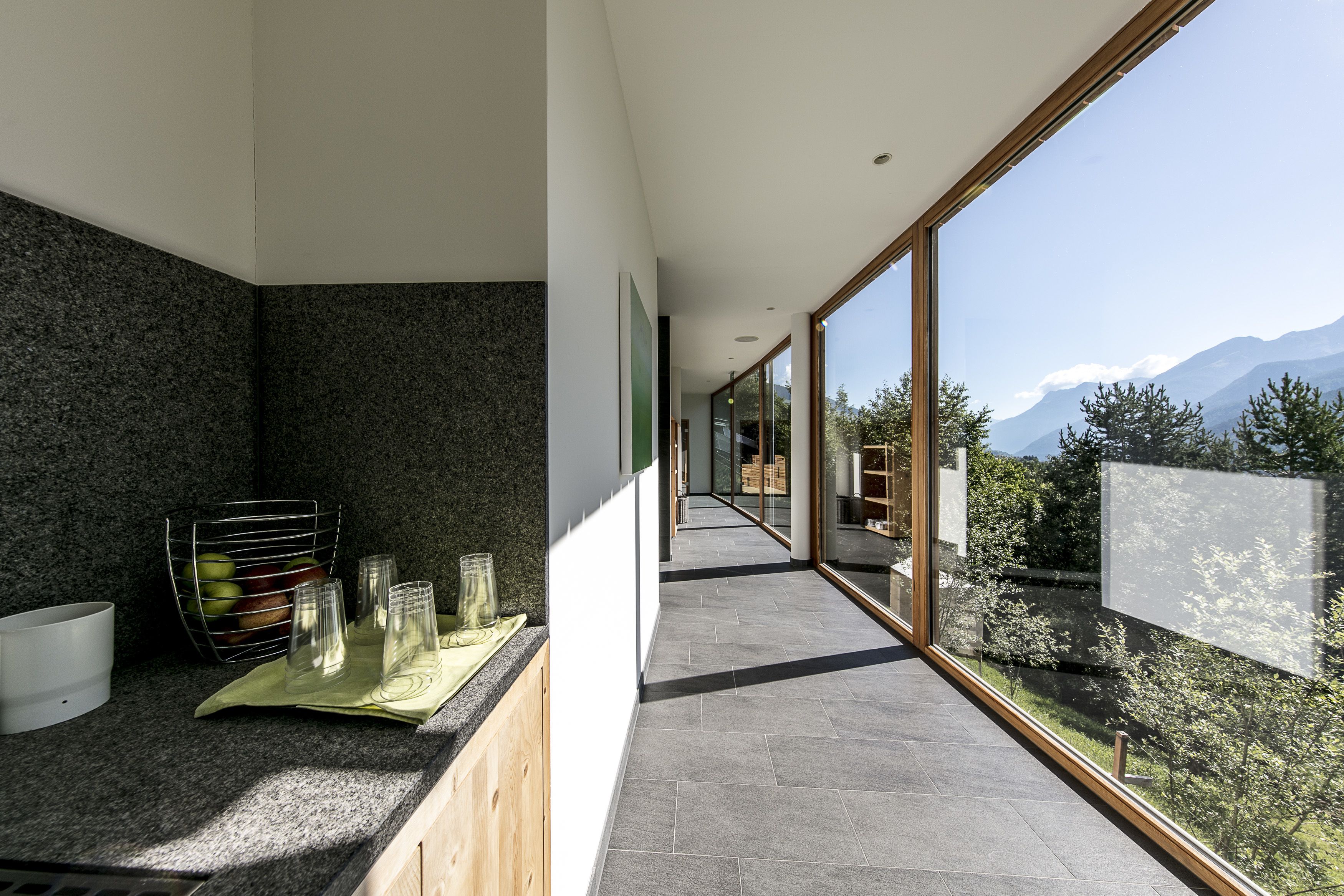 Una cocina moderna con encimeras de granito, una frutera de alambre y vistas a un paisaje montañoso a través de amplias ventanas.