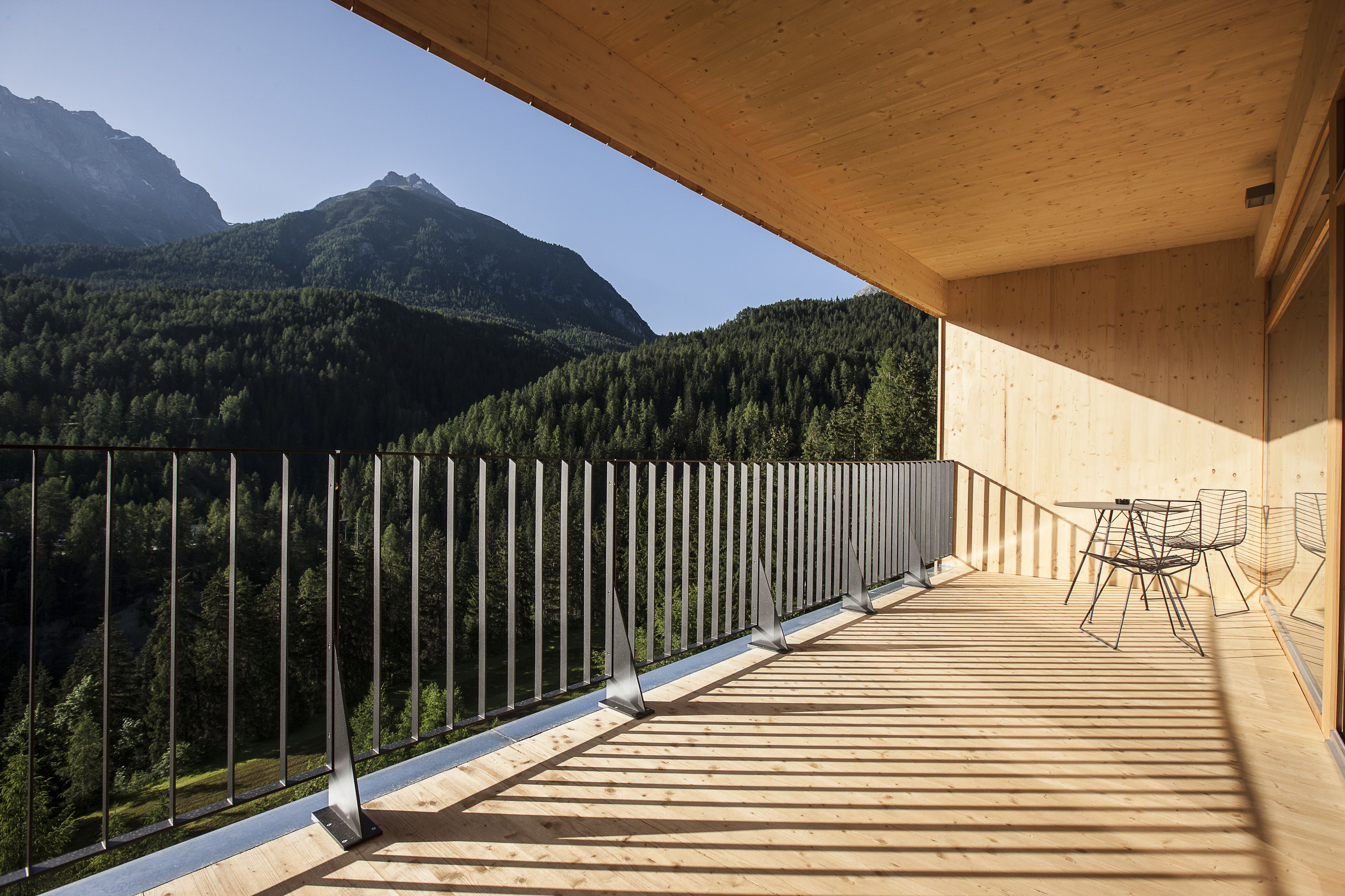 A wooden deck with a metal railing overlooking a forested valley and mountains.
