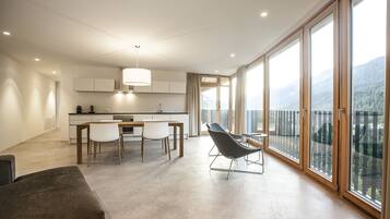 Une cuisine moderne avec des meubles blancs, un coin repas comprenant une table et des chaises, et de grandes portes-fenêtres coulissantes donnant sur un balcon avec vue sur les montagnes.